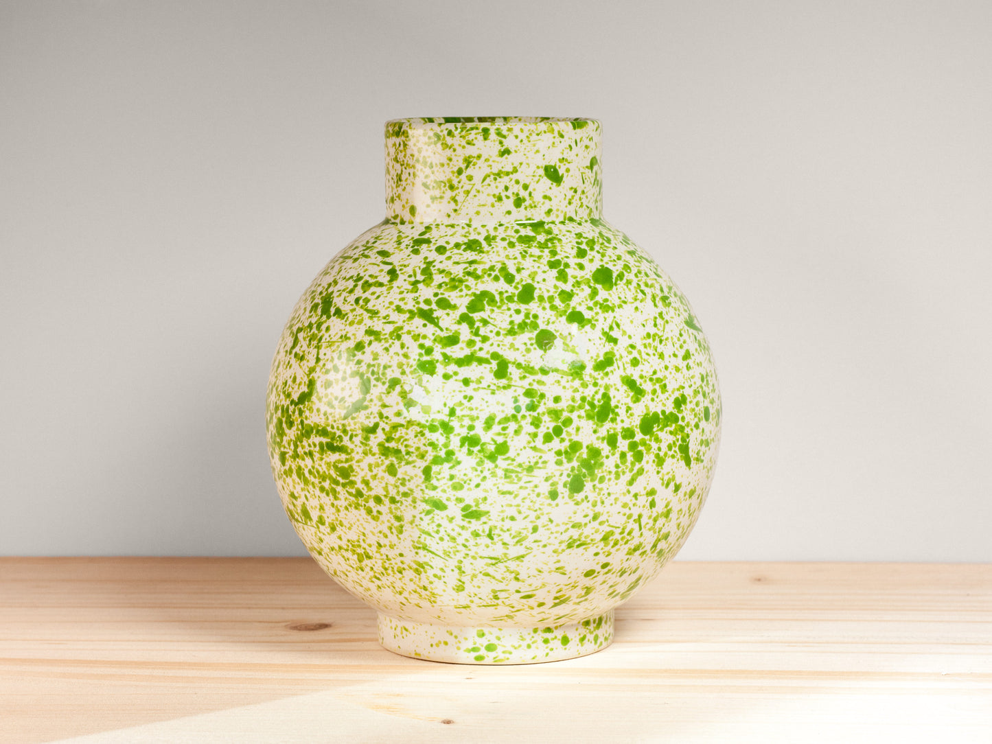 White and green ceramic vase on a wooden surface with a plain background.