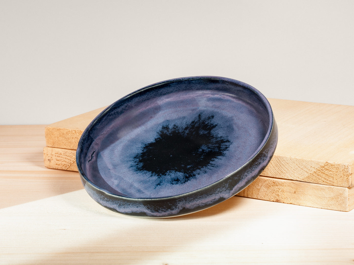 Blue ceramic plate with a black center on a wooden block against a light background
