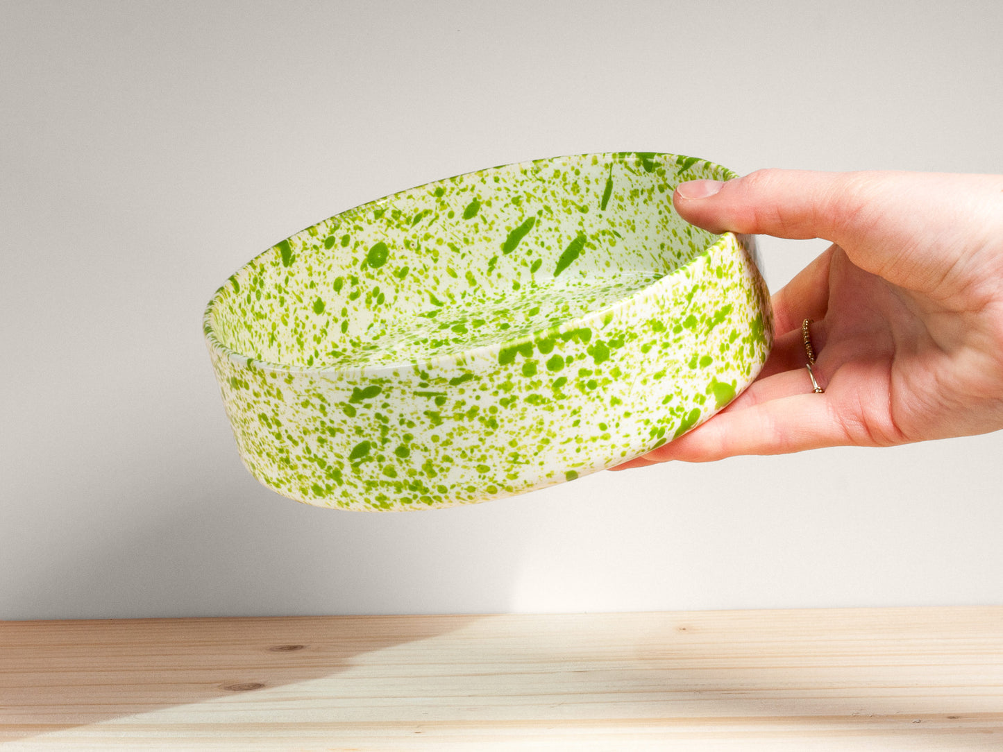 Hand holding a green and white patterned bowl against a light background