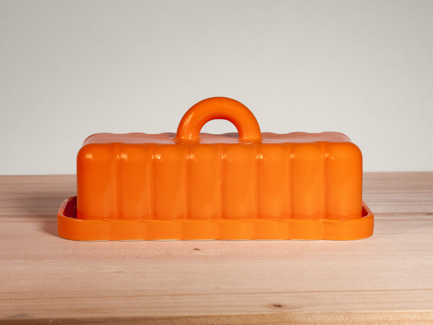 Orange ceramic butter dish with lid on a wooden surface
