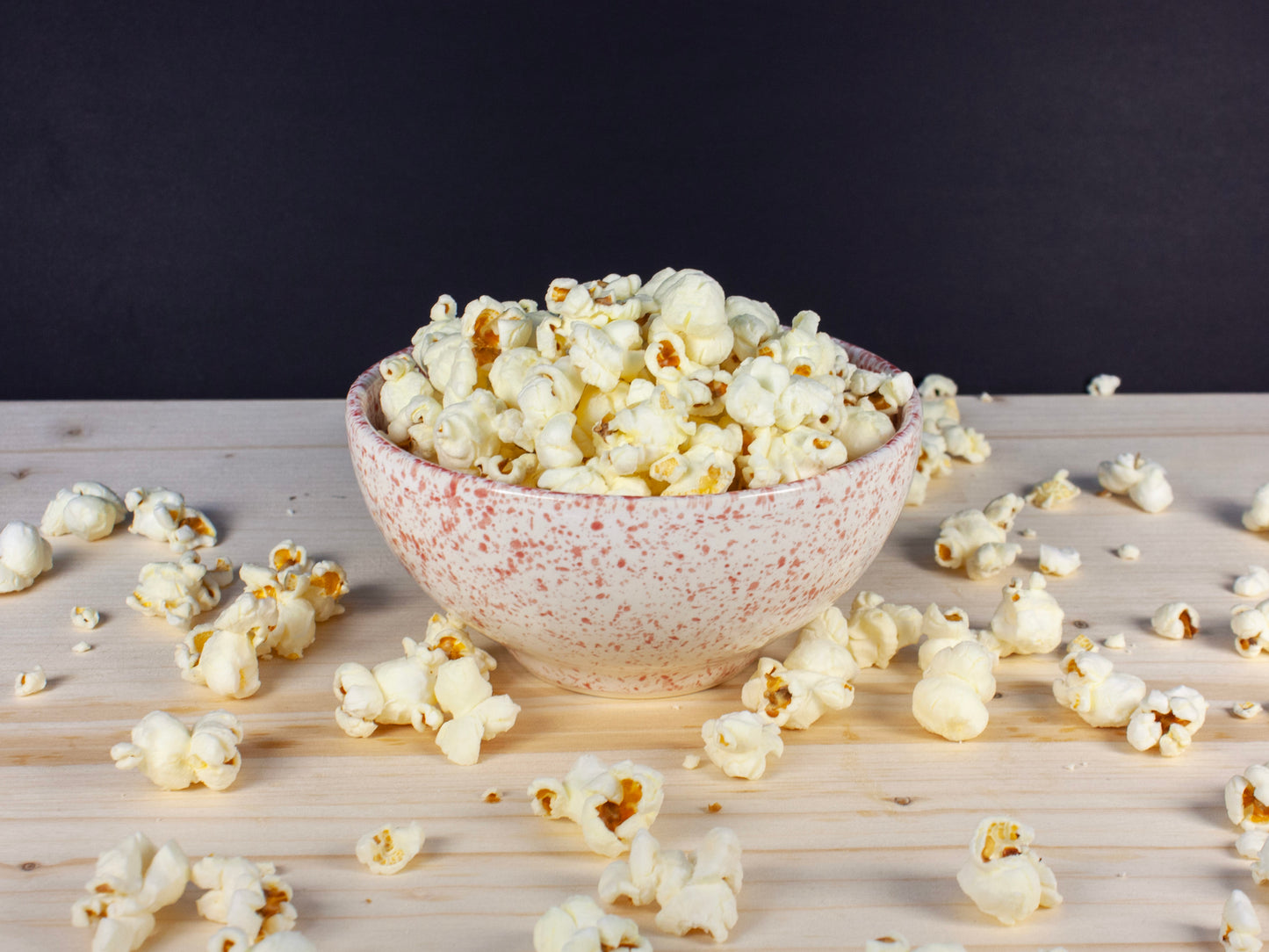 A ceramic bowl with a pink splattered design full of popcorn.