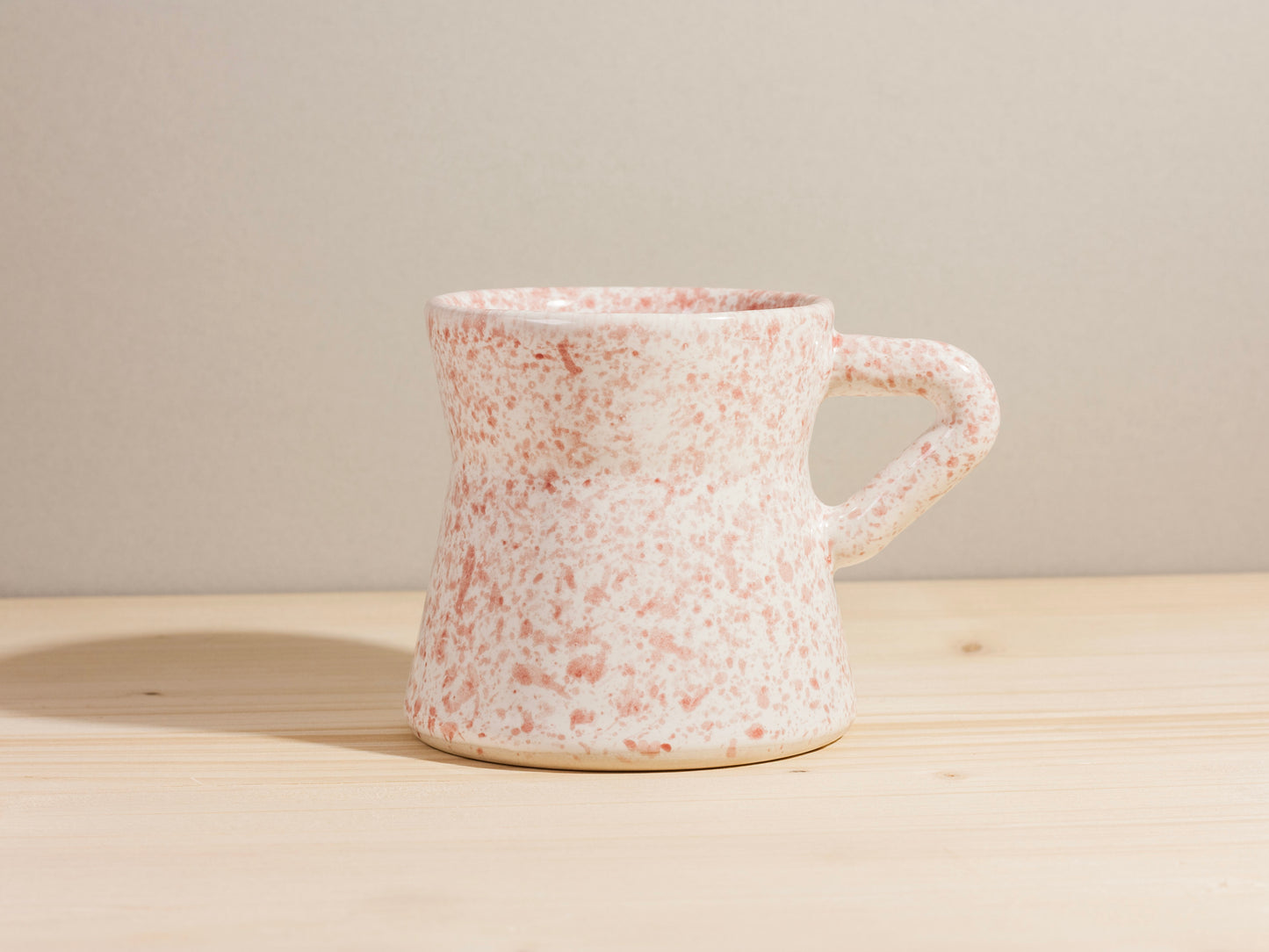 Speckled ceramic mug on a wooden surface with a neutral background