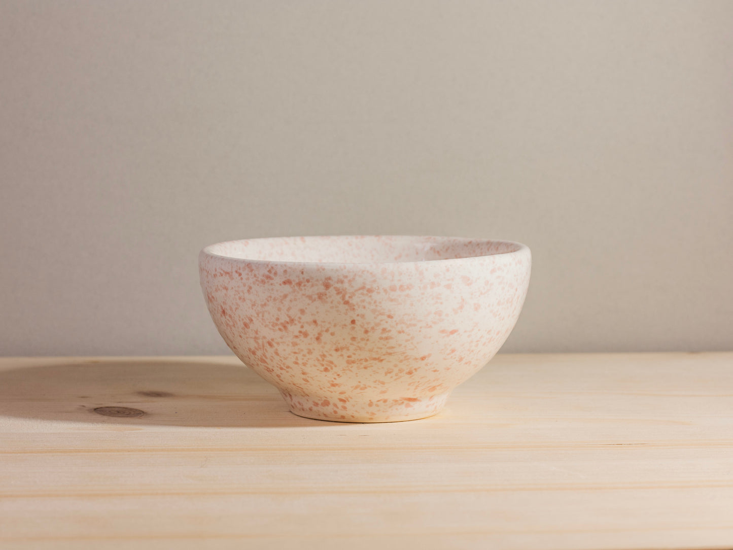 Speckled ceramic bowl on a wooden surface with a neutral background