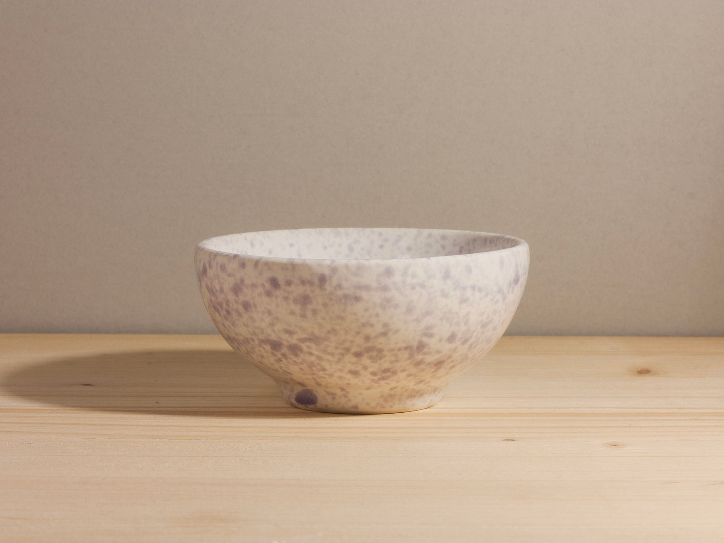 White and purple ceramic bowl on a wooden surface with a neutral background