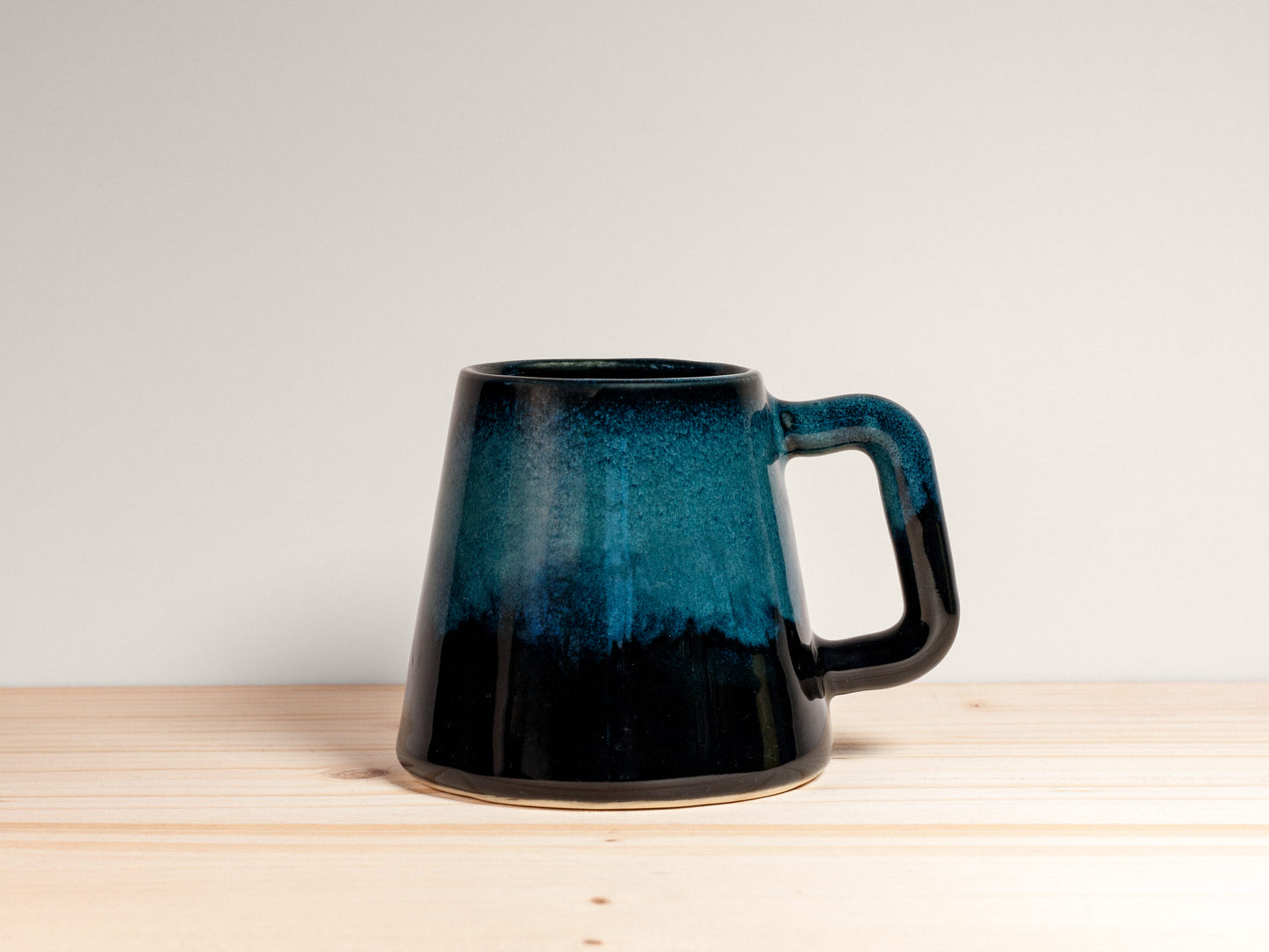 Dark teal ceramic mug on a wooden surface with a plain background.
