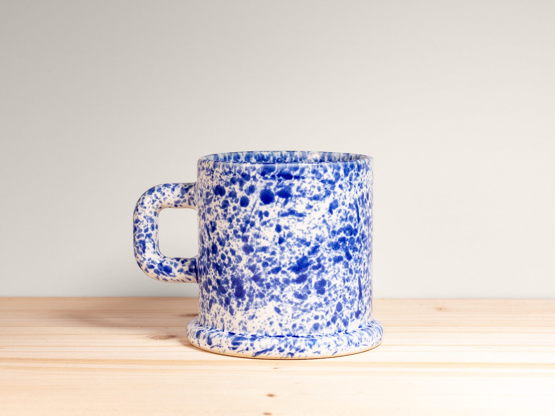 Blue and white speckled mug on a wooden surface with a light gray background