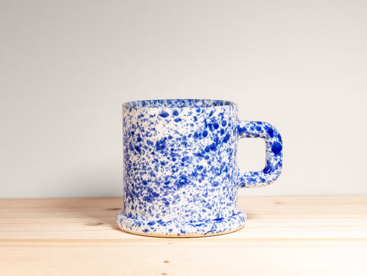 Blue and white speckled mug on a wooden surface with a light gray background