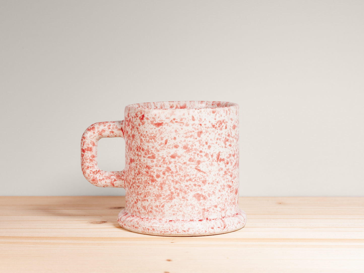 Speckled ceramic mug on a wooden surface with a light gray background