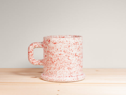 Speckled ceramic mug on a wooden surface with a light gray background