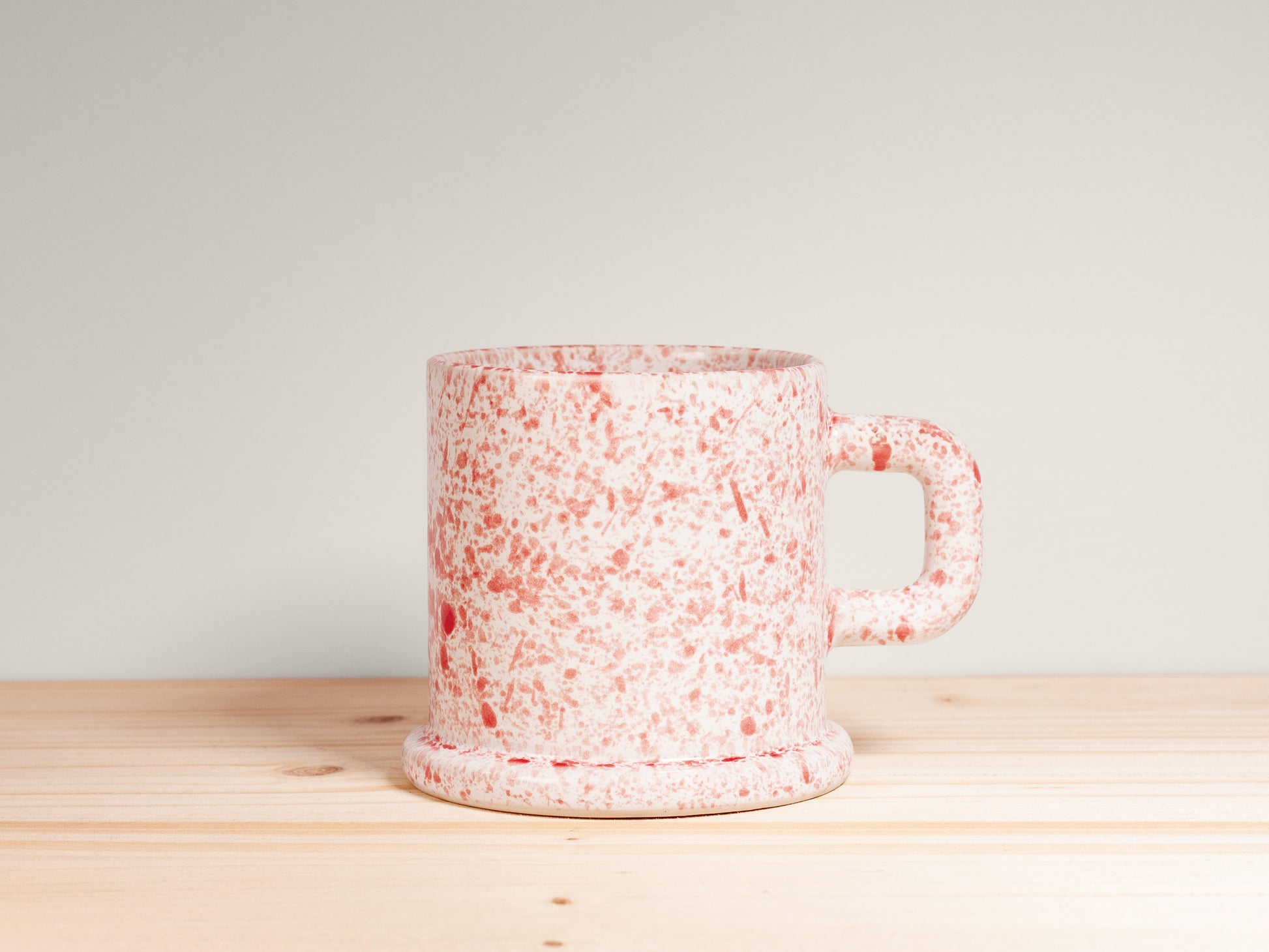 Speckled red and white ceramic mug on a wooden surface with a light gray background