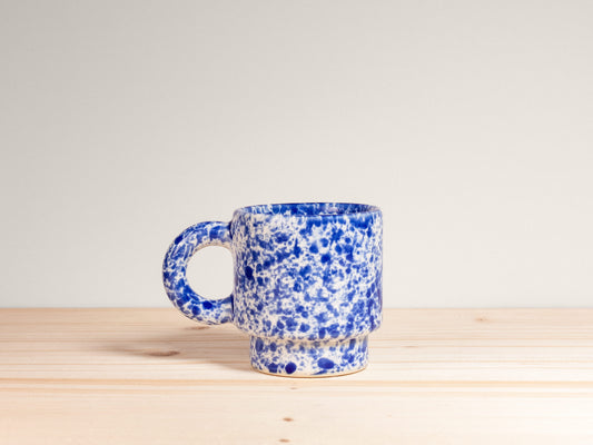 Blue and white speckled mug on a wooden surface with a light gray background