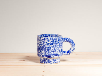 Blue speckled mug on a wooden surface with a light gray background