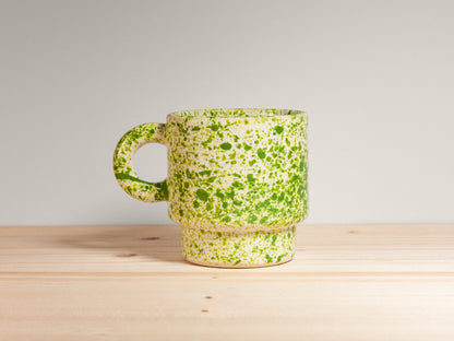 Green speckled ceramic mug on a wooden surface with a light gray background