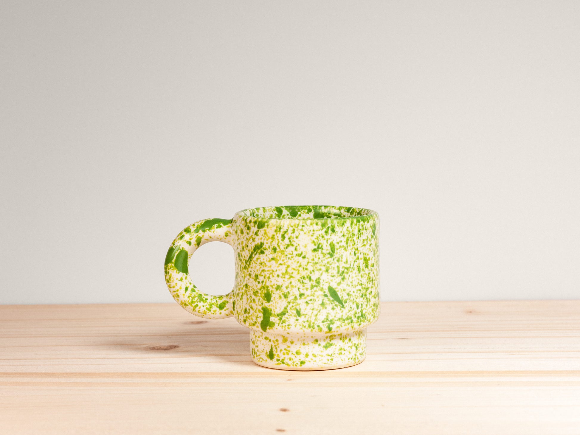 Green speckled mug on a wooden surface with a light gray background