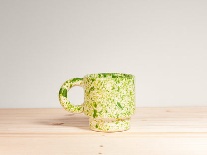 Green speckled mug on a wooden surface with a light gray background