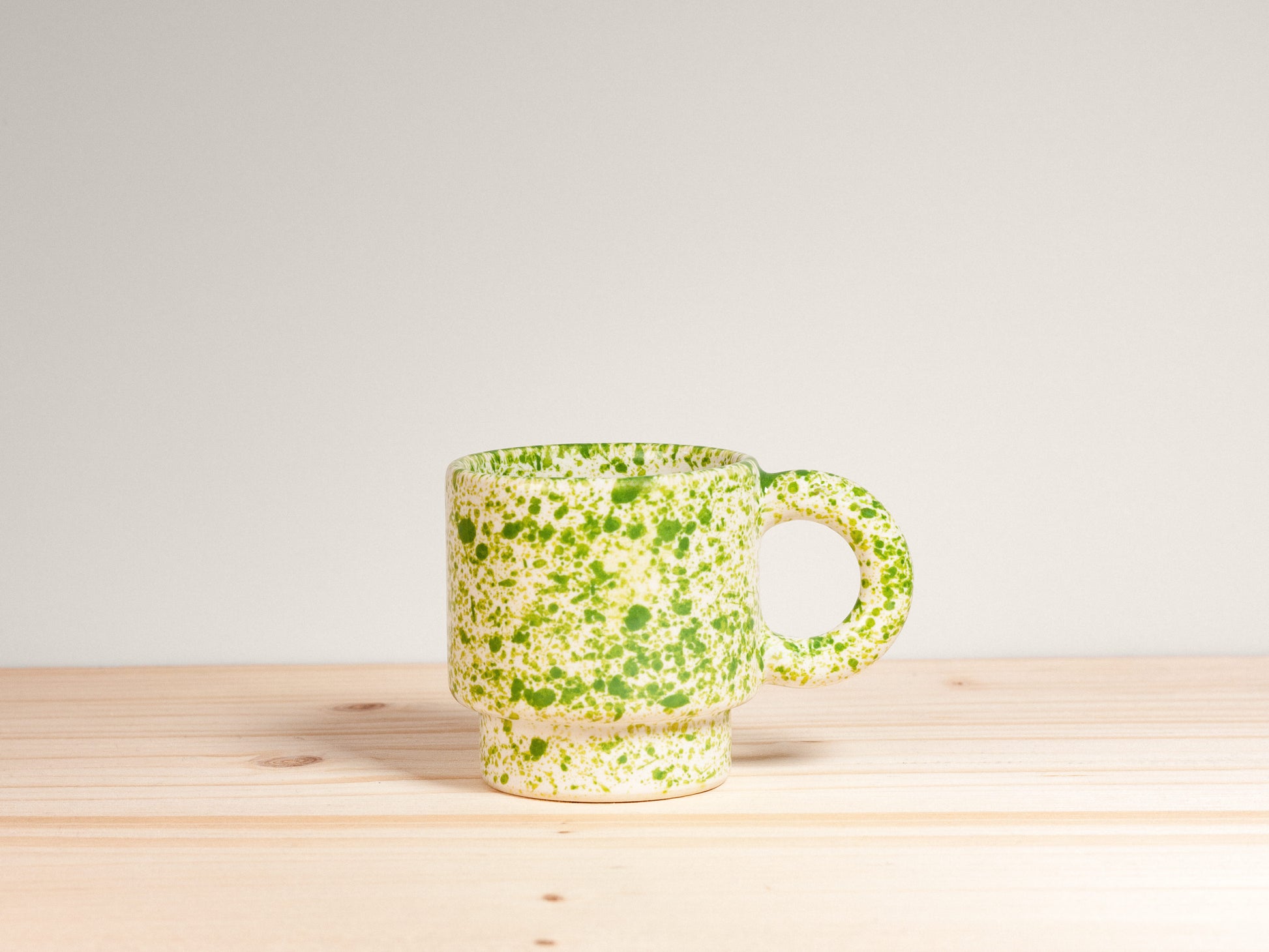 Green speckled mug on a wooden surface with a light gray background