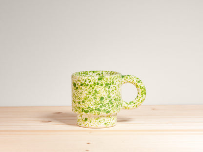 Green speckled mug on a wooden surface with a light gray background