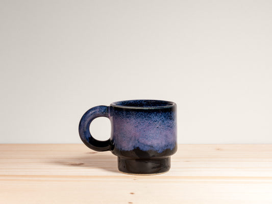 Small dark purple ceramic mug on a wooden surface with a plain background.