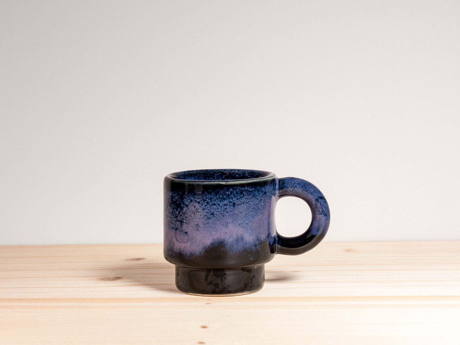 Small dark purple ceramic mug on a wooden surface with a plain background.