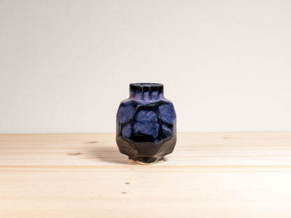 Black and blue ceramic vase on a wooden surface with a white background