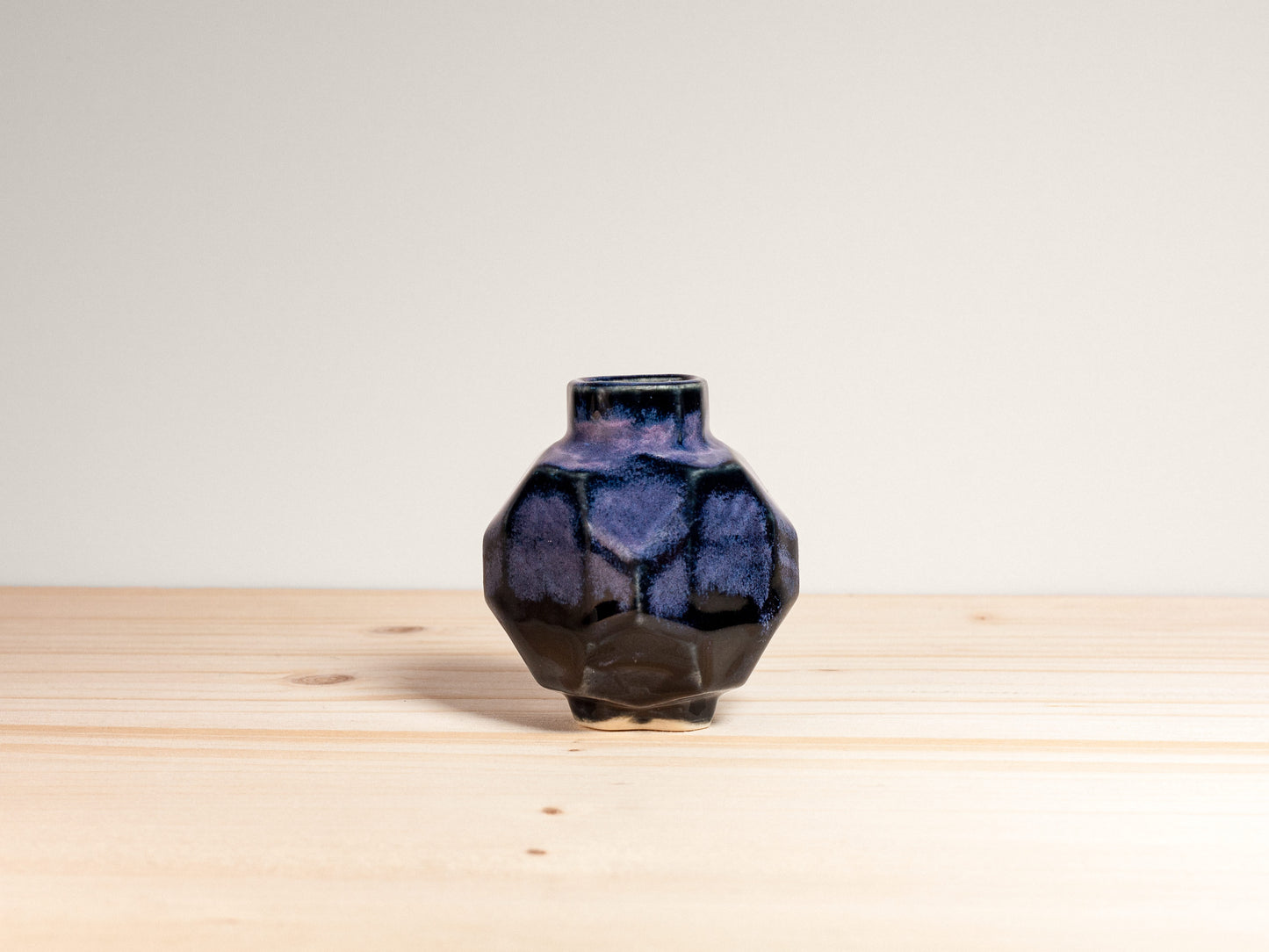 Faceted purple vase on a wooden surface with a light gray background