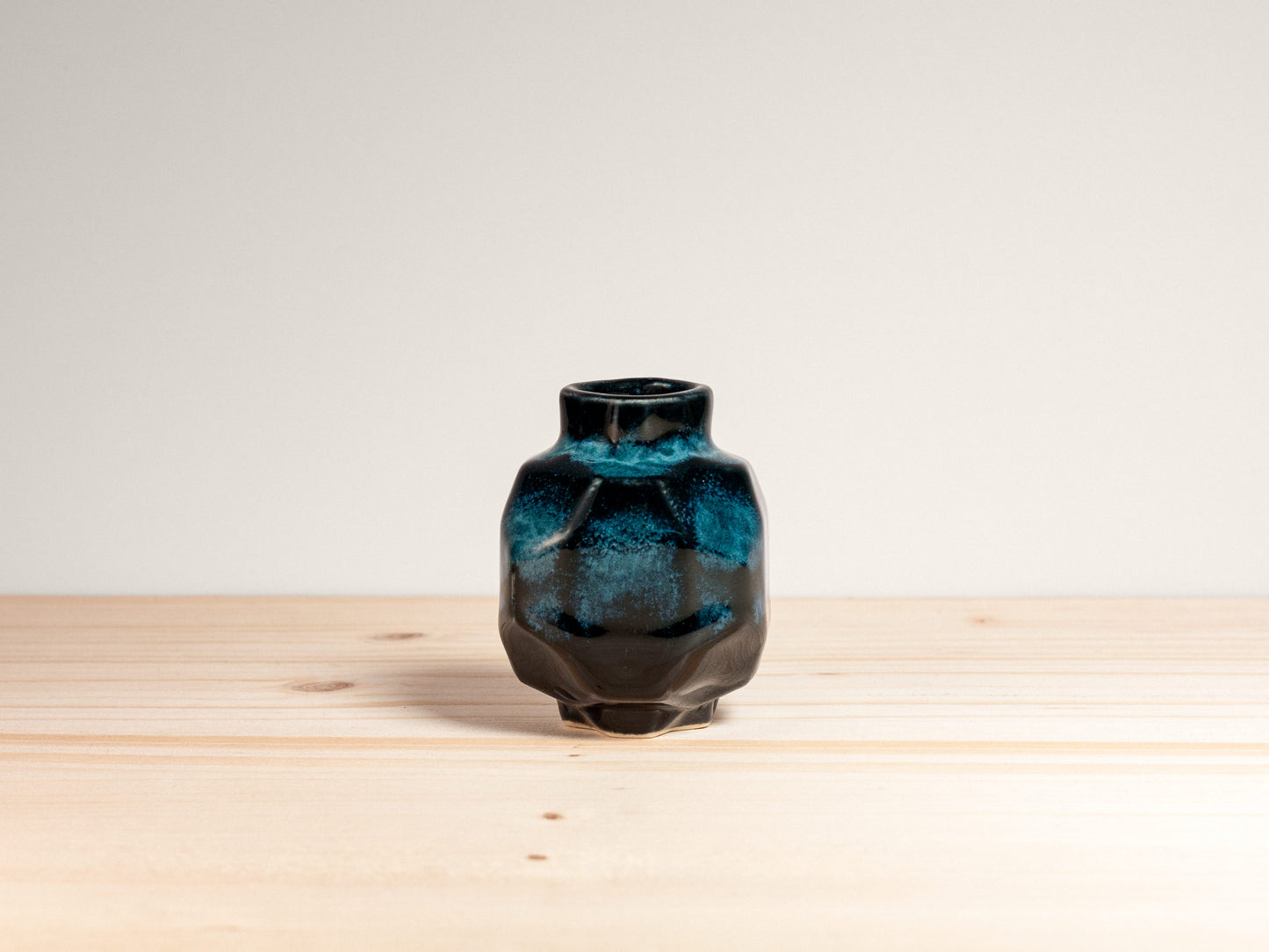 Small geometric dark teal ceramic vase on a wooden surface.