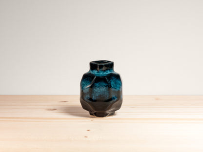 Small geometric dark teal ceramic vase on a wooden surface.