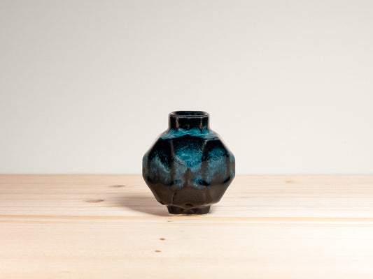 Small geometric dark teal ceramic vase on a wooden surface.