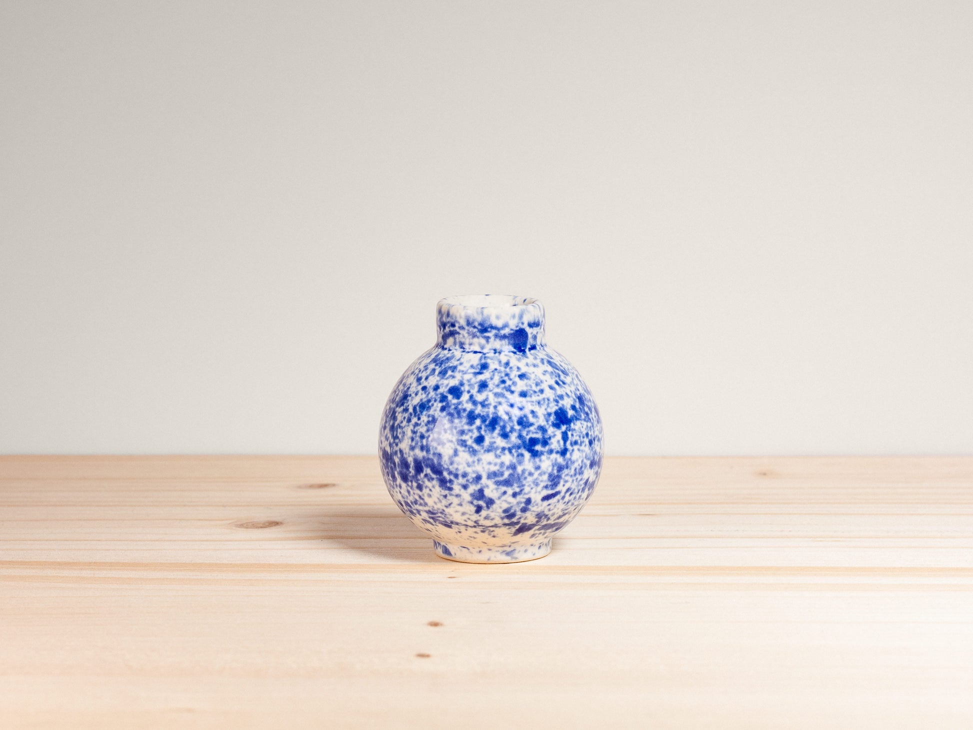 Blue and white speckled vase on a wooden surface with a light gray background