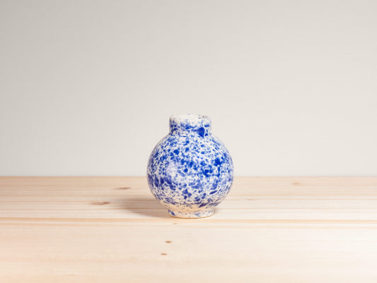Blue and white speckled vase on a wooden surface with a light gray background