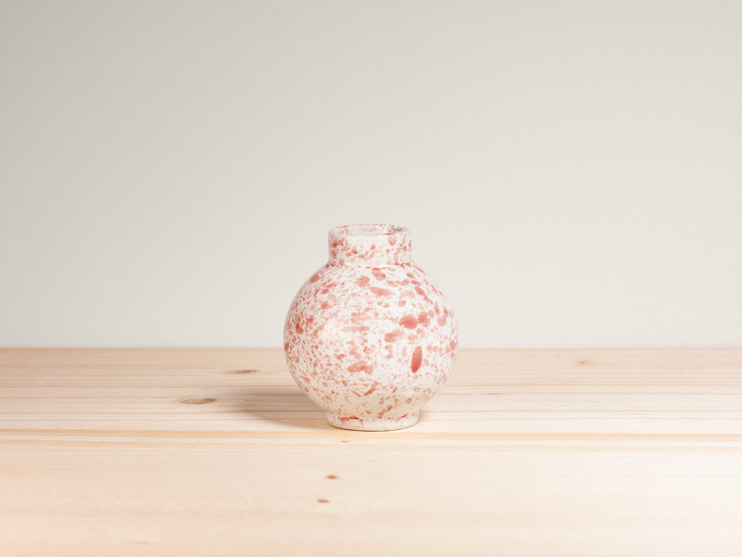Speckled pink and white vase on a wooden surface with a light gray background