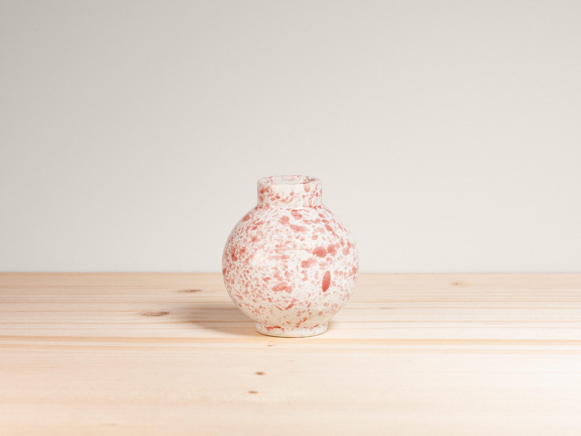 Speckled pink and white vase on a wooden surface with a light gray background