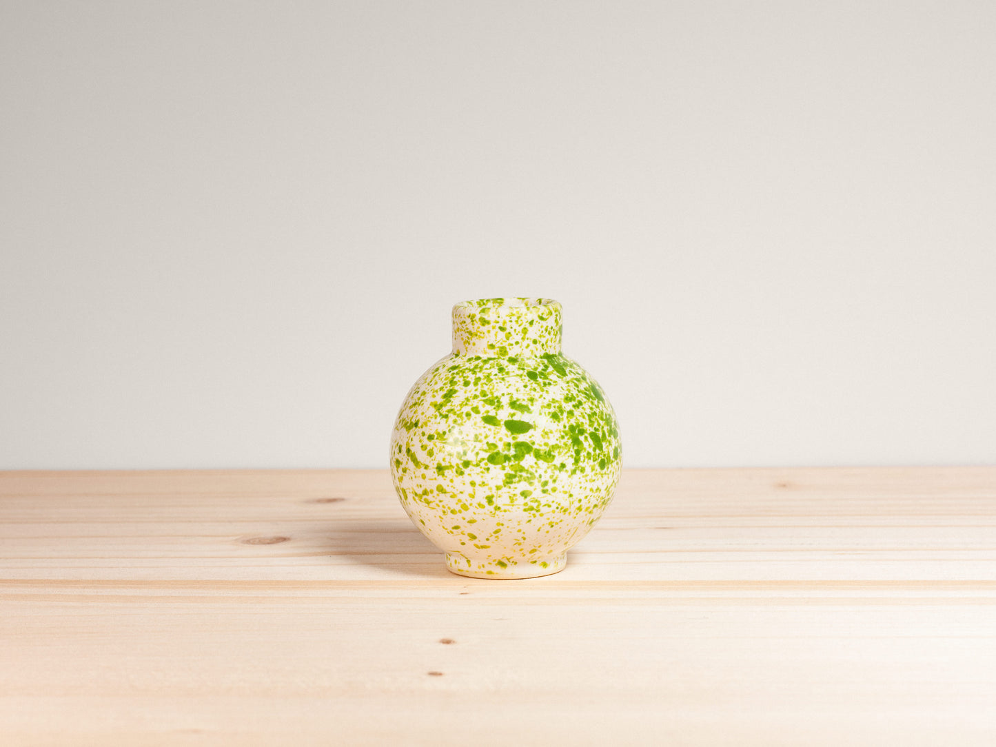 Small green and white ceramic vase on a wooden surface with a plain background.