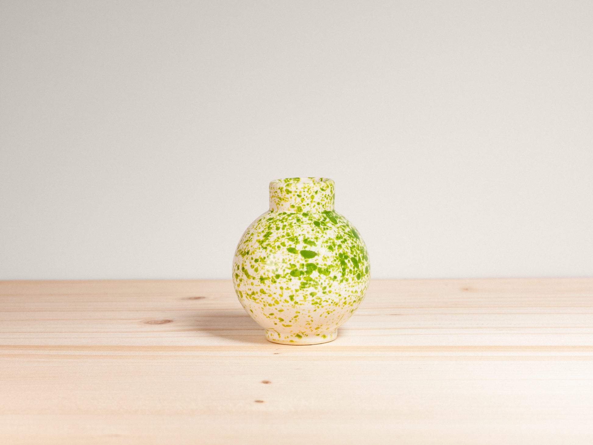 Small green and white ceramic vase on a wooden surface with a plain background.