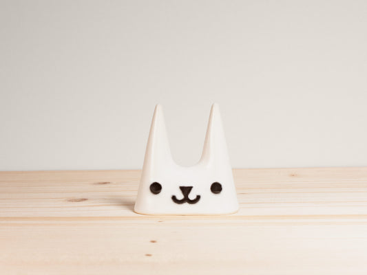 White ceramic cat-shaped ring holder with a face on a wooden surface