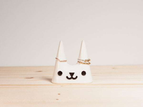 White ceramic cat-shaped ring holder with a face on a wooden surface
