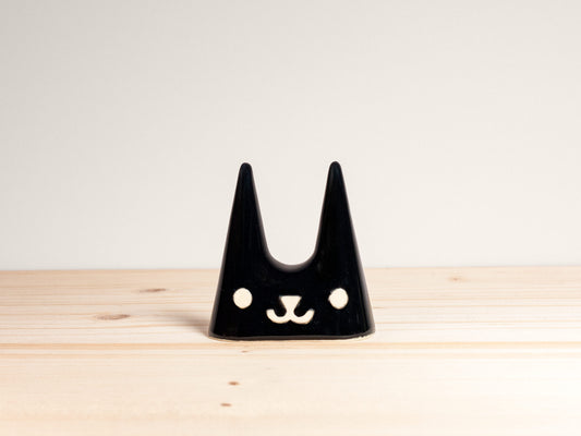 Black cat-shaped ring holder on a wooden surface with a light gray background