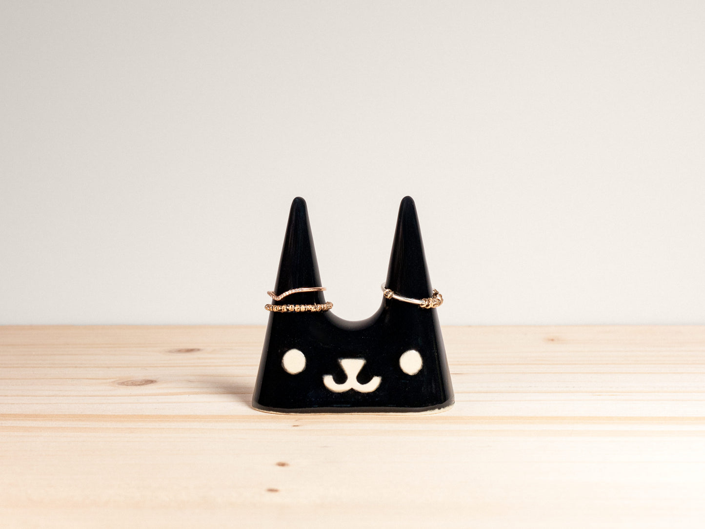 Black cat-shaped jewelry holder on a wooden surface with a light gray background