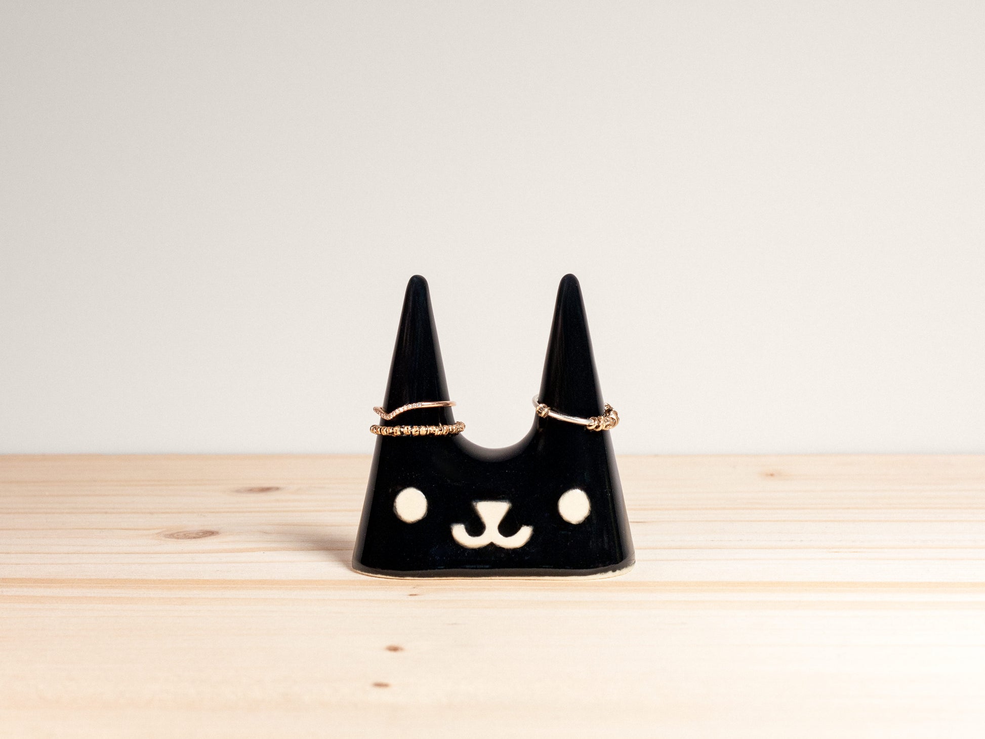 Black cat-shaped jewelry holder on a wooden surface with a light gray background
