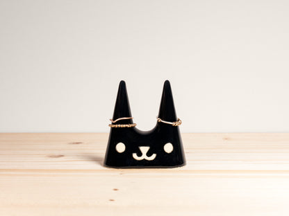 Black cat-shaped jewelry holder on a wooden surface with a light gray background