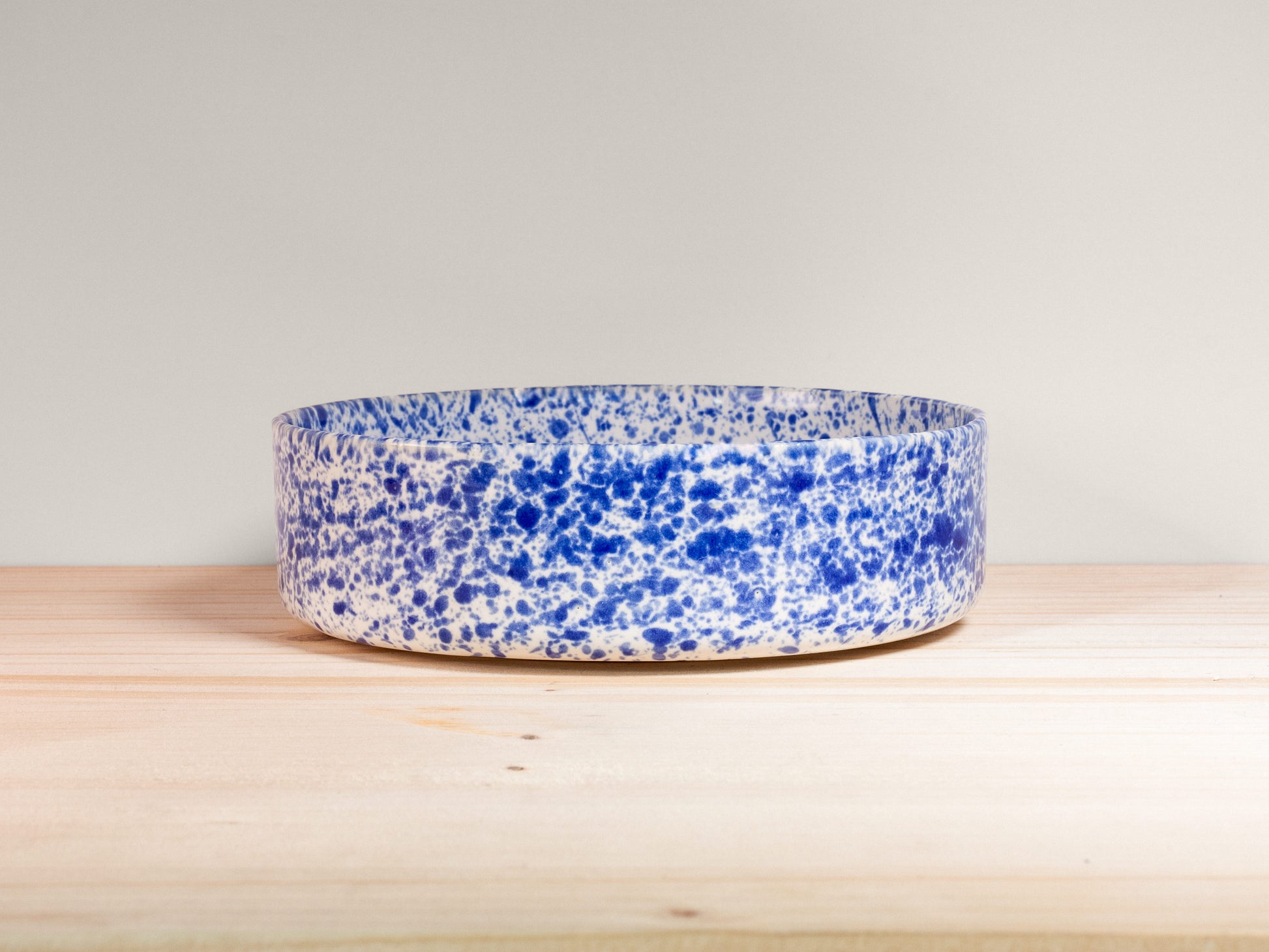 Blue and white speckled bowl on a wooden surface with a light gray background