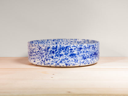 Blue and white speckled bowl on a wooden surface with a light gray background
