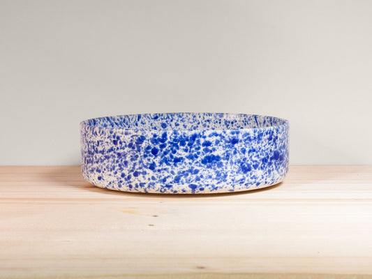 Blue and white speckled bowl on a wooden surface with a light gray background