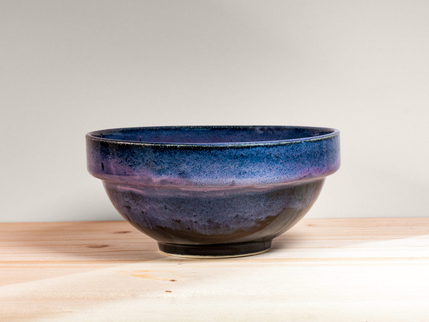Dark purple ceramic bowl on a wooden surface with a light gray background