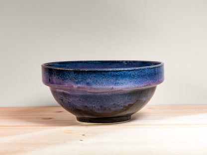 Dark purple ceramic bowl on a wooden surface with a light gray background