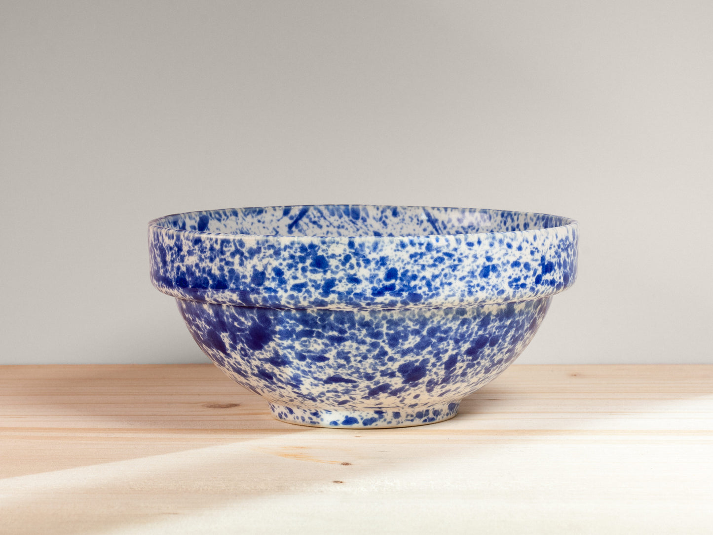 Blue and white speckled ceramic bowl on a wooden surface with a light gray background