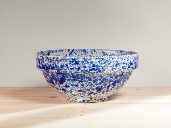 Blue and white speckled ceramic bowl on a wooden surface with a light gray background