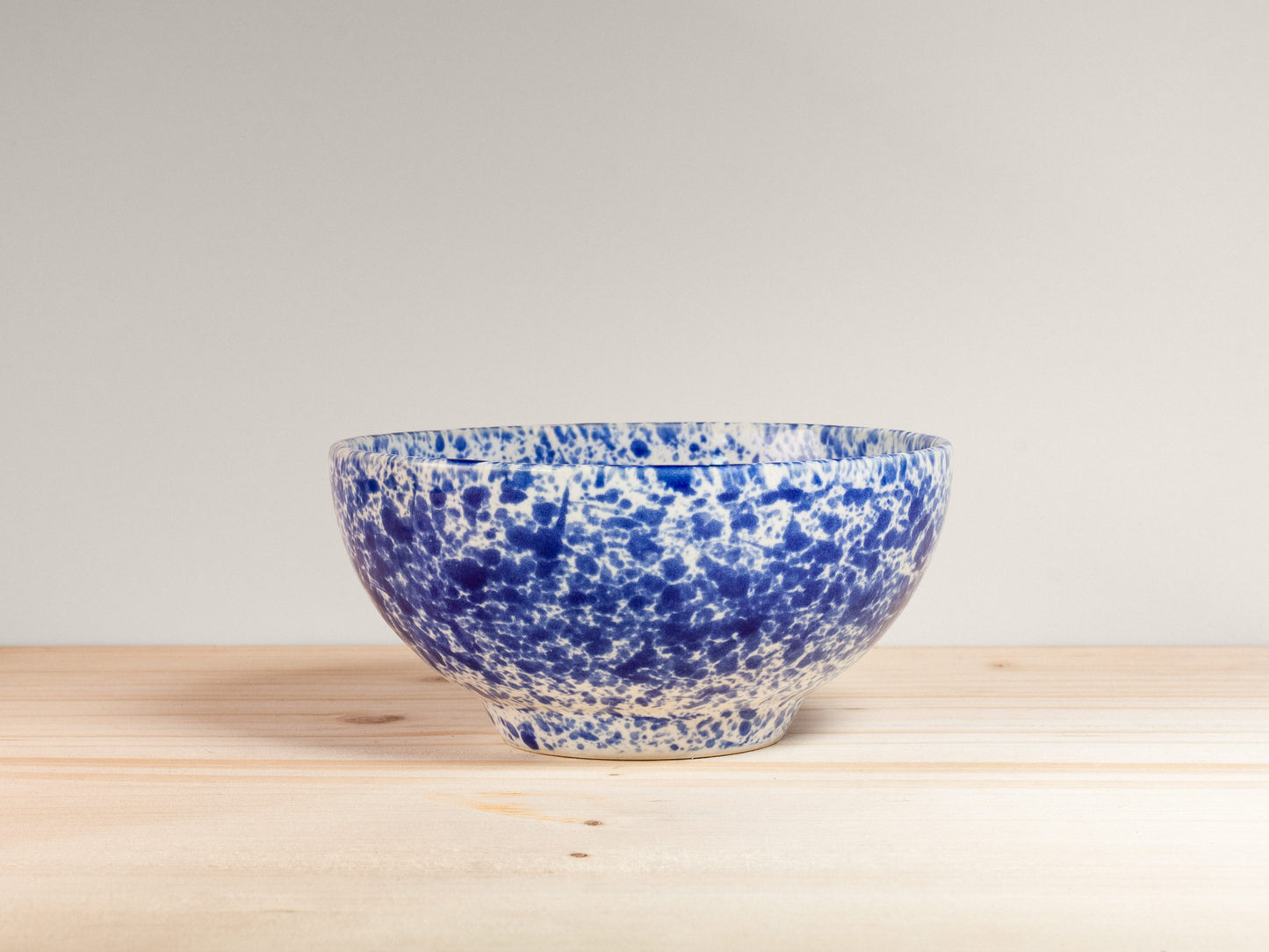 Blue and white speckled ceramic bowl on a wooden surface with a light gray background