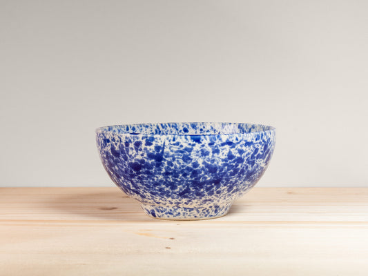 Blue and white speckled ceramic bowl on a wooden surface with a light gray background