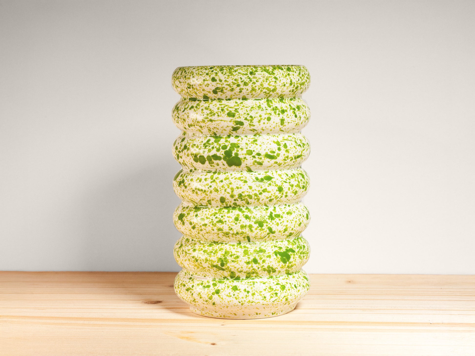 White and green ceramic vase on a wooden surface with a light gray background